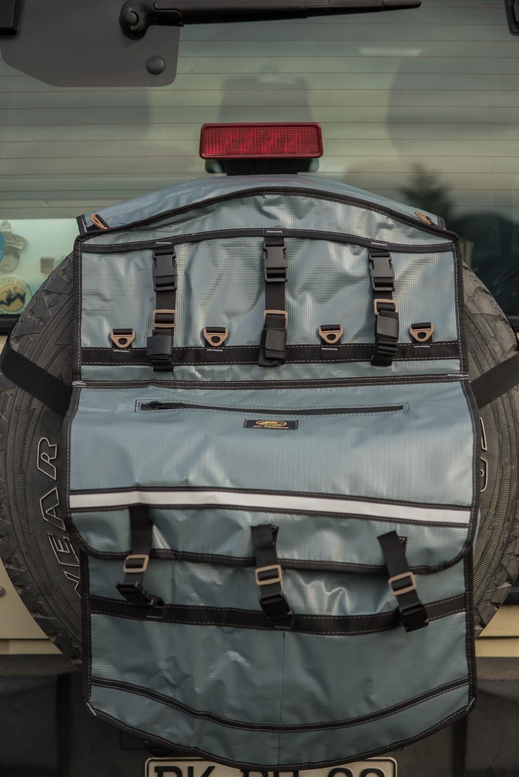 Bolso Para Neumático gris con múltiples correas y compartimentos fijado a una rueda trasera de vehículo