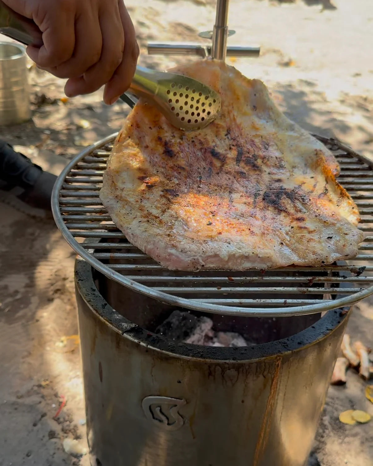 Carne cocinándose sobre parrilla inoxidable Humos para camping en exterior con pinzas de metal