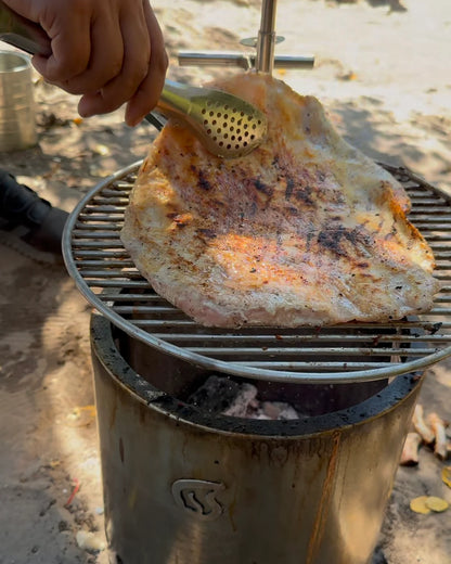 Carne cocinándose sobre parrilla inoxidable Humos para camping en exterior con pinzas de metal