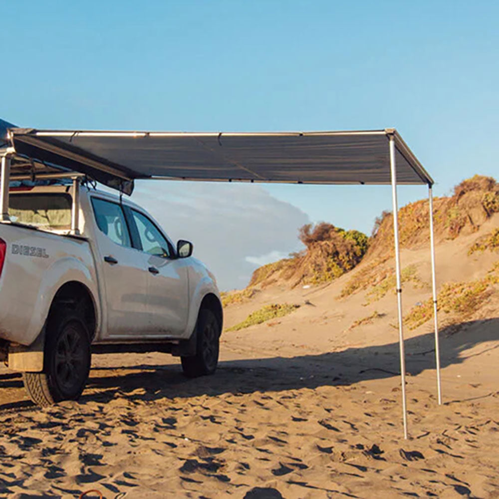 Toldo Lateral TRIBU instalado en la playa, proporcionando sombra a un vehículo 4x4